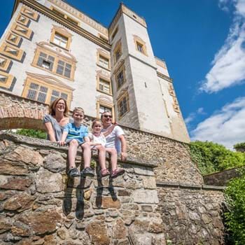 Fürstenbau Veste Oberhaus ©Pedagrafie Eine Familie an einer Mauer, im Hintergrund der Fürstenbau mit Kapellenerker.